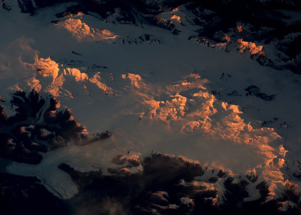 Sunset over a mountain range as seen from the International Space Station, with rugged peaks silhouetted against the fading light of the atmosphere.